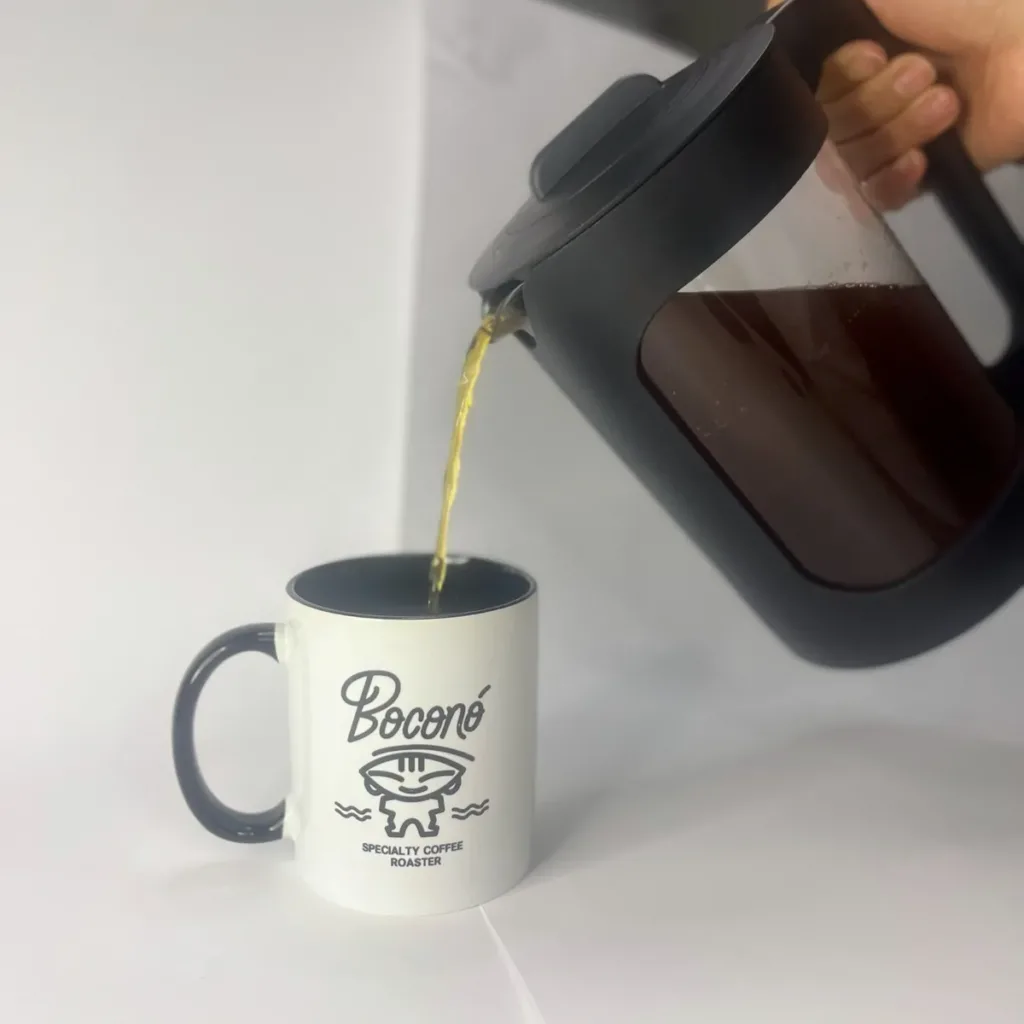 Una mano sirve cold brew desde la jarra negra de 1,5 litros de Boconó en una taza blanca con el logotipo de Boconó, sobre fondo blanco