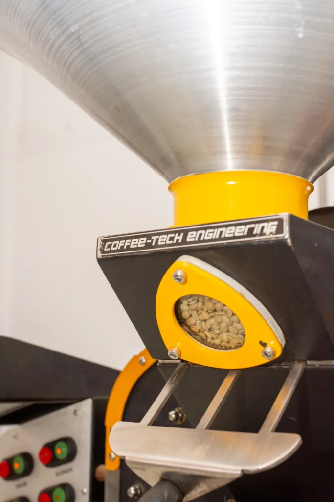 Tolva de acero de la tostadora Coffee-Tech de Boconó con el visor amarillo lleno de café verde, listo para caer al tambor