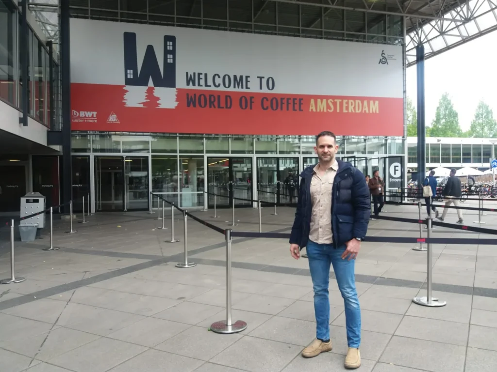 Carlos Núñez, tostador de Boconó, delante del cartel de bienvenida del World of Coffee de Ámsterdam 2018, la feria de la Specialty Coffee Association