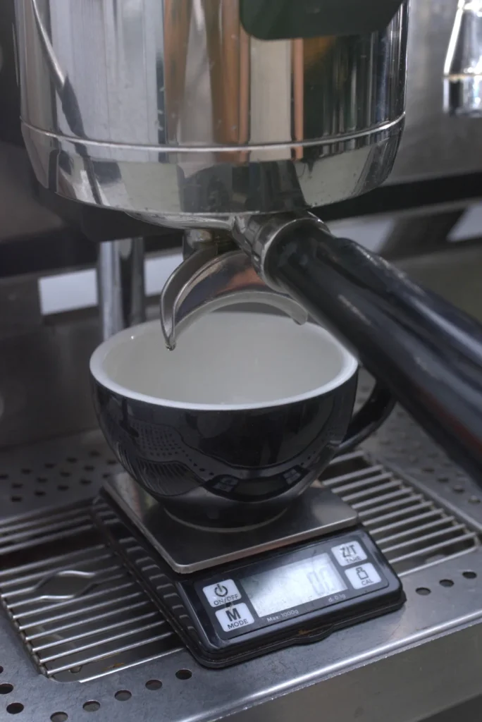 Taza negra sobre una báscula de café, colocada bajo el portafiltros de una máquina de espresso