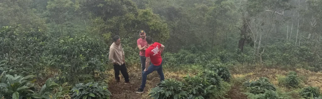 Niebla sobre el monte y cafetos en la finca La Neblina, en Zea (Mérida, Venezuela), con Carlos Núñez de Boconó de espaldas, con la camiseta roja de la marca, hablando con dos personas entre las plantas