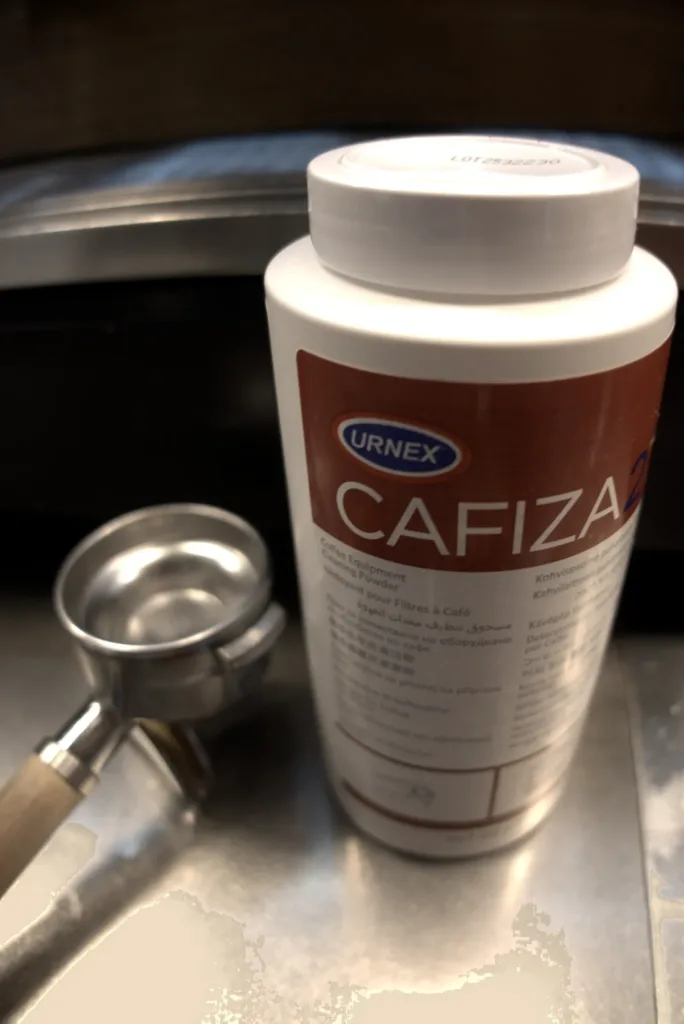 Bote de Cafiza 2 de Urnex apoyado en la máquina de espresso de dos grupos del tostadero de Boconó, con los portafiltros puestos