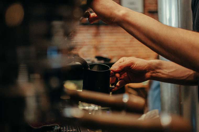 Barista texturizando la leche en una jarra con el vaporizador de la máquina de espresso