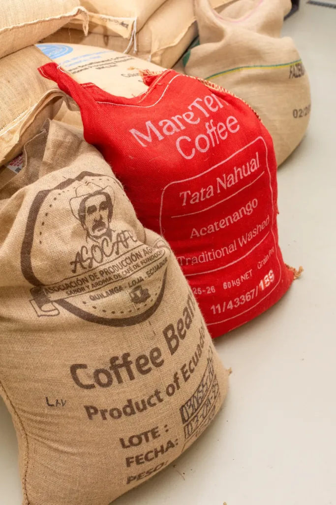 Dos sacos de café verde en el tostadero de Boconó, uno de yute con la leyenda Product of Ecuador y el número de lote y la fecha escritos a mano, y otro rojo de un lote de Acatenango