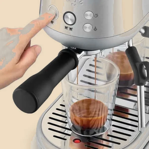 Una mano pulsa los botones de dosis mientras el espresso cae dentro de un vaso de cristal.