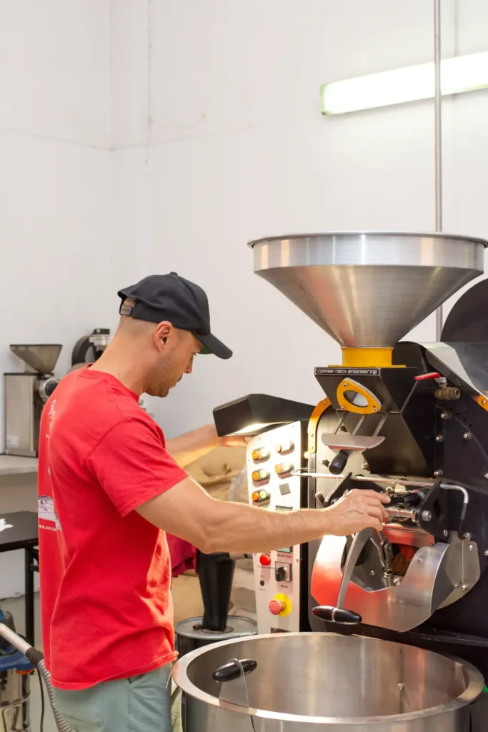 Gastón Saldivia abre la compuerta de la tostadora Coffee-Tech y el café recién tostado cae a la bandeja de enfriamiento, en el tostadero de Boconó en Madrid