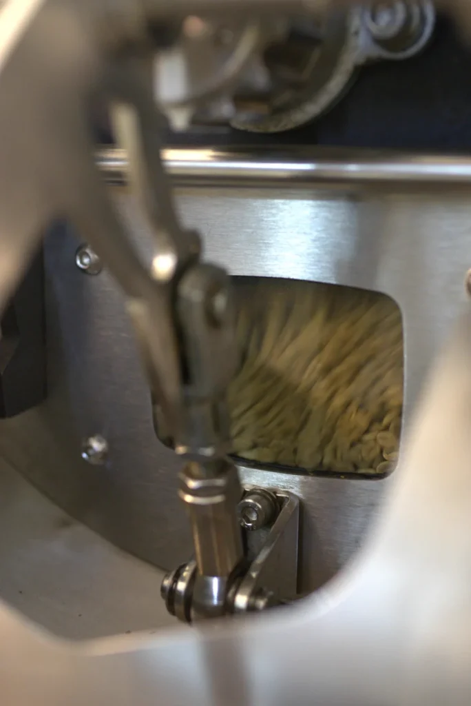Café verde girando dentro del tambor de la tostadora, visto a través de la mirilla, en el tostadero de Boconó