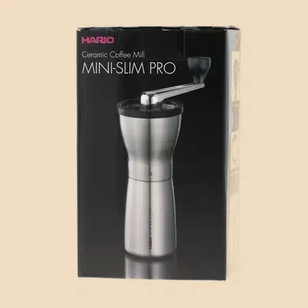 Caja de cartón del molinillo manual Hario, con la fotografía del producto y el nombre del modelo impresos.